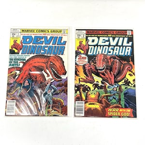 Puede incluir: Dos cómics vintage de "Devil Dinosaur". Las portadas presentan un gran dinosaurio rojo, con el título en azul. El número 5 muestra una escena de batalla con el texto "Neither man nor monster can long survive in the kingdom of the ants!" El número 2 dice "War with the Spider God!"