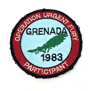 May include: Circular patch with the text "OPERATION URGENT FURY" in white on a red border. The center features "GRENADA" and "1983" with a green island map on a light blue background. The text "PARTICIPANT" is at the bottom.