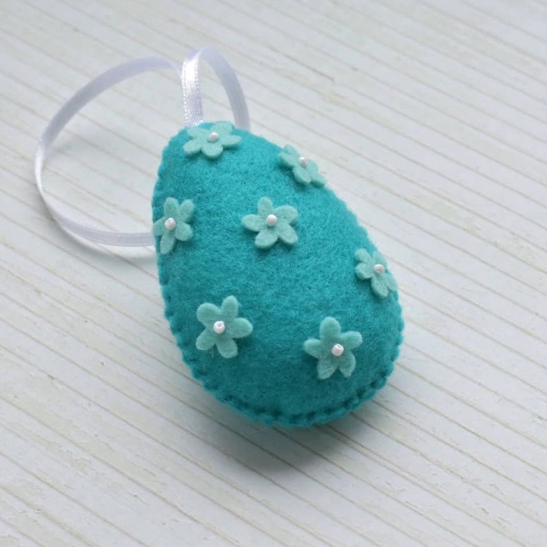 May include: Teal felt Easter egg ornament with white felt flowers and white pearl beads.