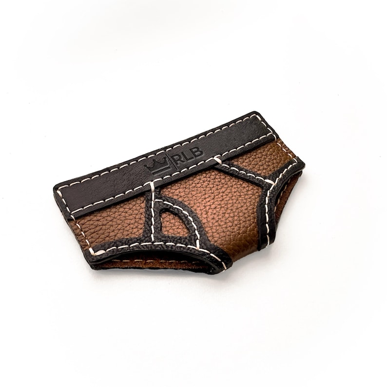 May include: A brown and black leather accessory with white stitching. The accessory has a textured surface and a dark brown top with the letters "RLB" and a crown logo. The item is on a white background.