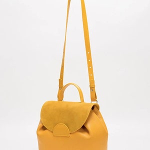 May include: A yellow leather satchel bag with a suede flap and a top handle. The bag has a long adjustable shoulder strap.