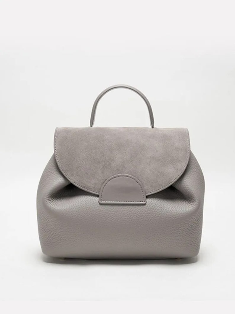 May include: A gray leather backpack with a suede flap and a top handle.