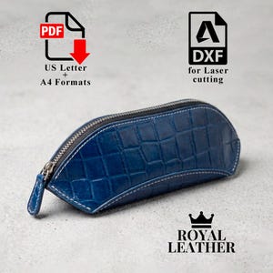 Può includere: Un astuccio in pelle blu con stampa coccodrillo, chiusura con zip argentata e cuciture bianche. Il testo include PDF US Letter + A4 Formats, DXF for laser cutting e Royal Leather con un'icona a forma di corona.