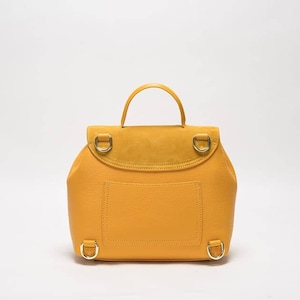 May include: A mustard yellow leather backpack with a suede flap and gold hardware. The backpack has a small pocket on the front and adjustable straps.