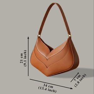 K&ouml;nnte beinhalten: Eine braune Schultertasche mit einem einzigartigen, blattartigen Design. Die Tasche ist 34 cm breit, 21 cm hoch und 7 cm dick. Sie hat einen einzelnen Riemen und goldfarbene Beschl&auml;ge. Die Tasche ist aus glattem Material gefertigt.