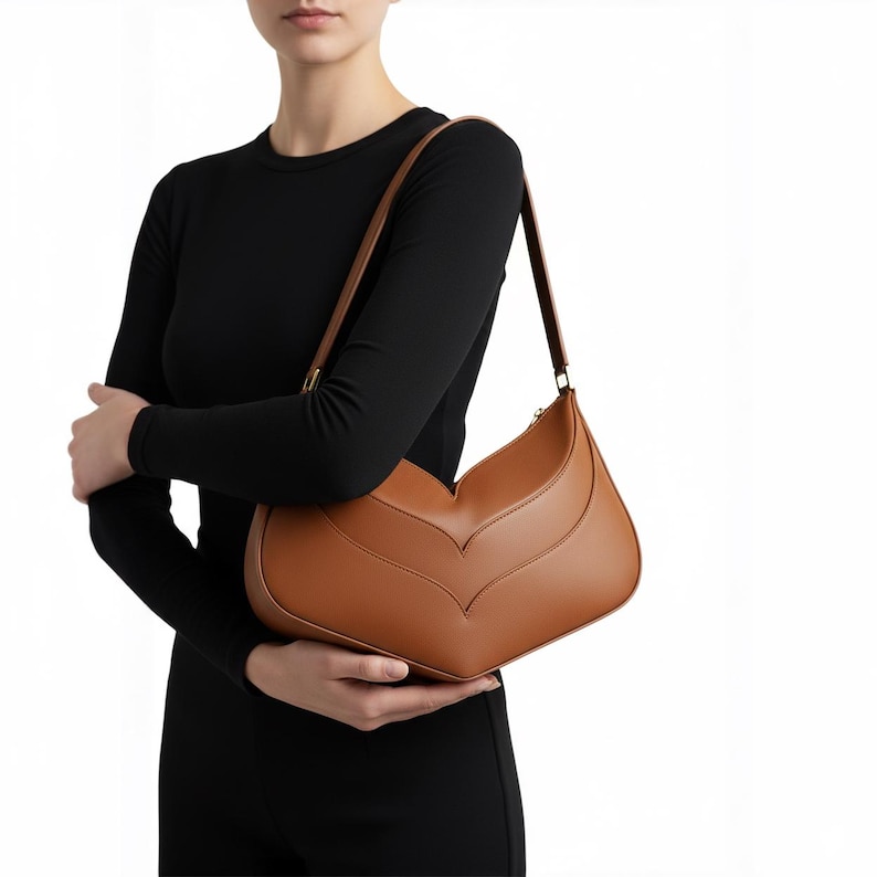 K&ouml;nnte beinhalten: Hellbraune Leder-Umh&auml;ngetasche mit einem einzigartigen Chevron-Design. Die Tasche hat einen langen Riemen und einen goldenen Rei&szlig;verschluss. Die Tasche hat eine hellbraune Farbe und eine glatte Textur. Ein stilvolles Accessoire.