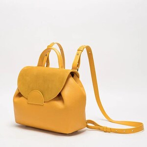 May include: A mustard yellow leather backpack with a suede flap and adjustable straps.