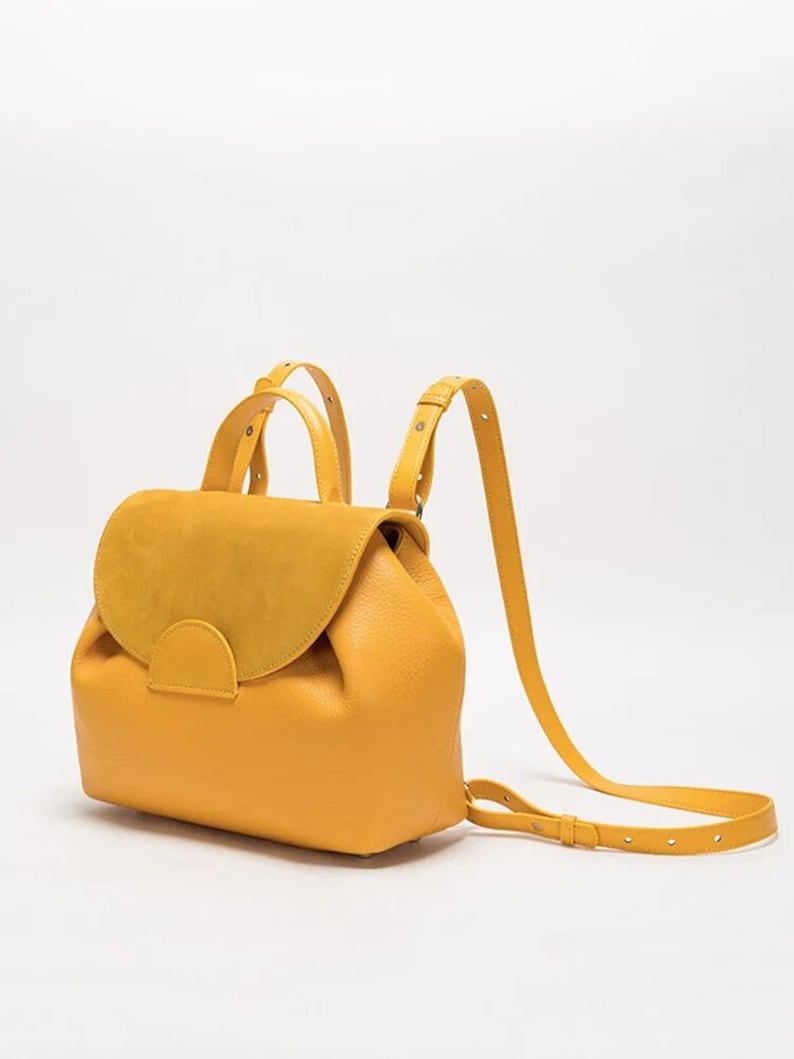 May include: A mustard yellow leather backpack with a suede flap and adjustable straps.