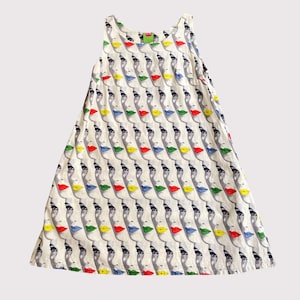 May include: A sleeveless A-line dress in an off-white color featuring a repeating pattern of stylized faces in profile. Each face is rendered in black and gray with lips colored in alternating shades of bright red, yellow, and blue.