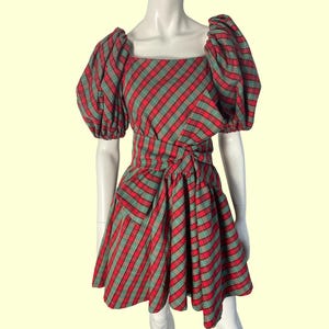 May include: A red and green plaid dress with a square neckline and puffed sleeves. The dress has a fitted waist and a flared skirt. The fabric features a diagonal plaid pattern. The dress is displayed on a mannequin.