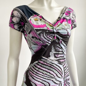 K&ouml;nnte beinhalten: Ein schwarz-wei&szlig;es Kleid mit einem rosa-blauen Schmetterlingsdruck. Das Kleid hat einen V-Ausschnitt und kurze &Auml;rmel.