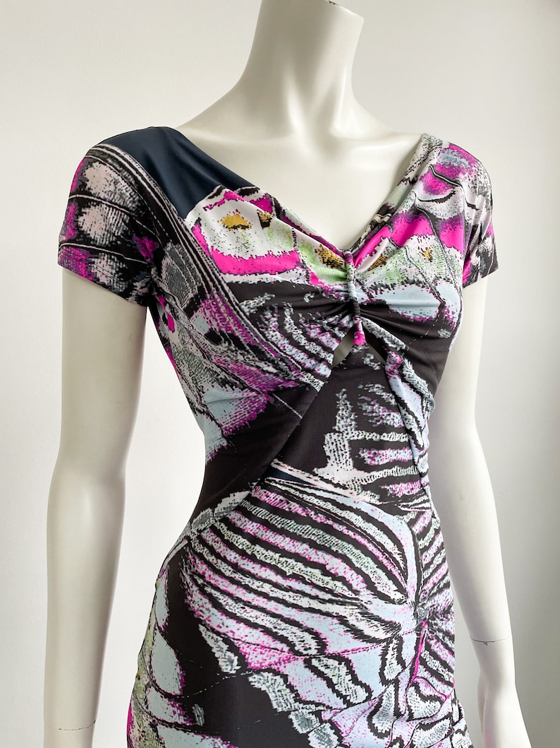 K&ouml;nnte beinhalten: Ein schwarz-wei&szlig;es Kleid mit einem rosa-blauen Schmetterlingsdruck. Das Kleid hat einen V-Ausschnitt und kurze &Auml;rmel.