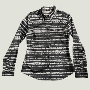 Puede incluir: Camisa de manga larga en blanco y negro con un patrón de rayas horizontales y texto. La camisa tiene un cuello clásico y puños abotonados. La tela parece ligera. Una prenda elegante.