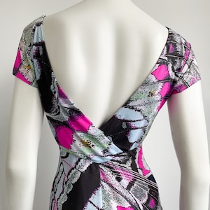 K&ouml;nnte beinhalten: Ein schwarz-wei&szlig;es Kleid mit einem abstrakten Schmetterlingsdruck in Pink, Blau und Gr&uuml;n. Das Kleid hat einen tiefen V-Ausschnitt und kurze &Auml;rmel.