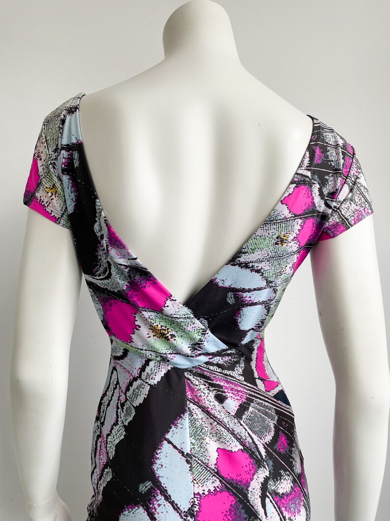 K&ouml;nnte beinhalten: Ein schwarz-wei&szlig;es Kleid mit einem abstrakten Schmetterlingsdruck in Pink, Blau und Gr&uuml;n. Das Kleid hat einen tiefen V-Ausschnitt und kurze &Auml;rmel.
