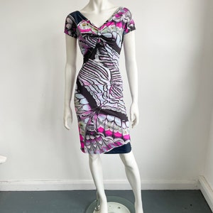 K&ouml;nnte beinhalten: Ein schwarzes, pinkfarbenes und blaues Kleid mit kurzen &Auml;rmeln und einem Schmetterlingsmuster. Das Kleid hat einen V-Ausschnitt und eine figurbetonte Silhouette.