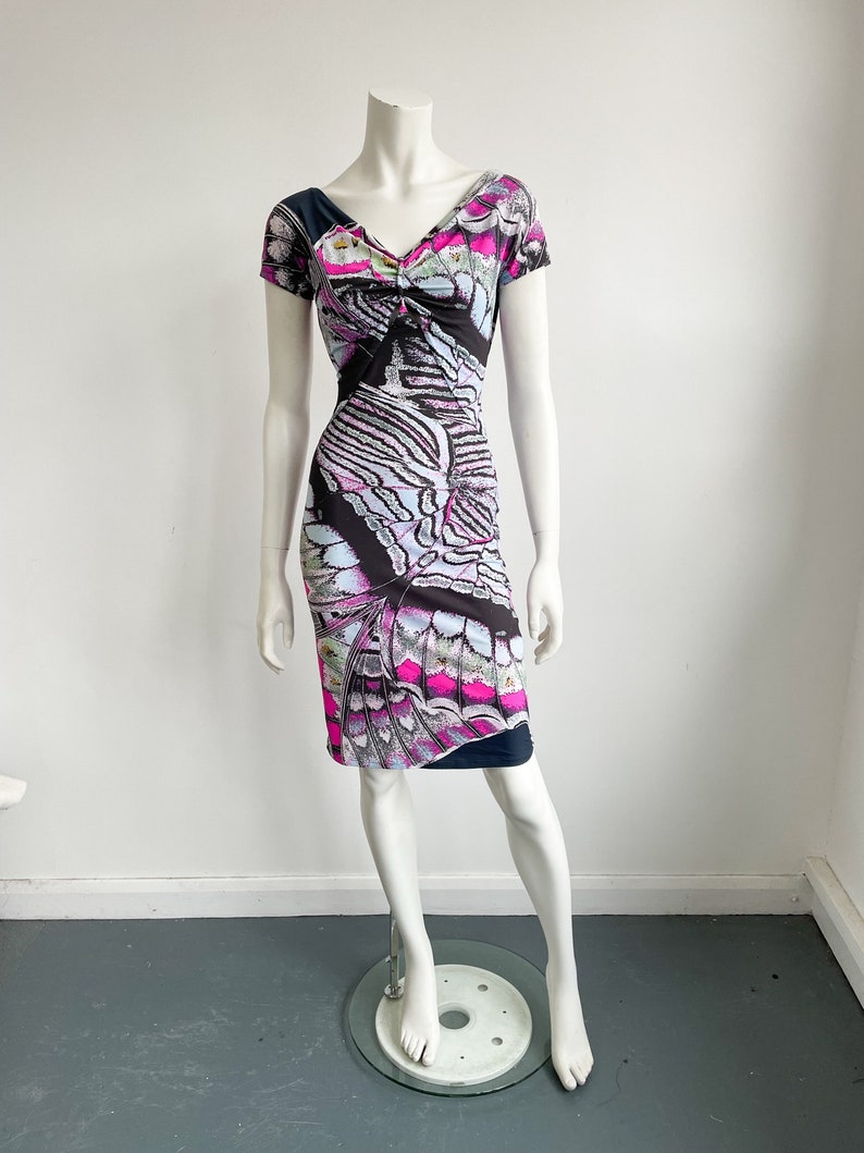 K&ouml;nnte beinhalten: Ein schwarzes, pinkfarbenes und blaues Kleid mit kurzen &Auml;rmeln und einem Schmetterlingsmuster. Das Kleid hat einen V-Ausschnitt und eine figurbetonte Silhouette.