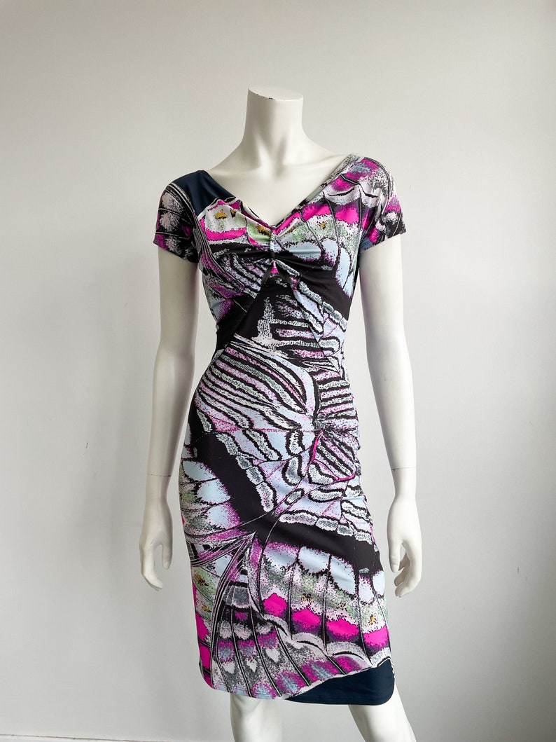 K&ouml;nnte beinhalten: Ein schwarzes, pinkfarbenes und blaues Kleid mit einem Schmetterlingsmuster. Das Kleid hat einen V-Ausschnitt und kurze &Auml;rmel.