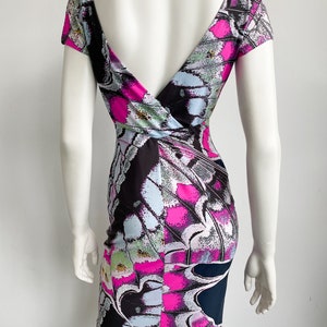 K&ouml;nnte beinhalten: Ein kurzes, figurbetontes Kleid mit tiefem V-Ausschnitt und einem bunten Schmetterlingsmuster. Das Kleid ist aus dehnbarem Stoff und hat eine figurbetonte Silhouette.