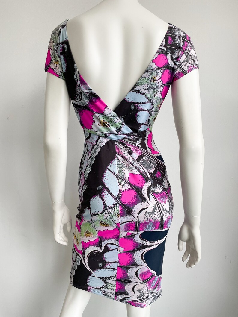 K&ouml;nnte beinhalten: Ein kurzes, figurbetontes Kleid mit tiefem V-Ausschnitt und einem bunten Schmetterlingsmuster. Das Kleid ist aus dehnbarem Stoff und hat eine figurbetonte Silhouette.