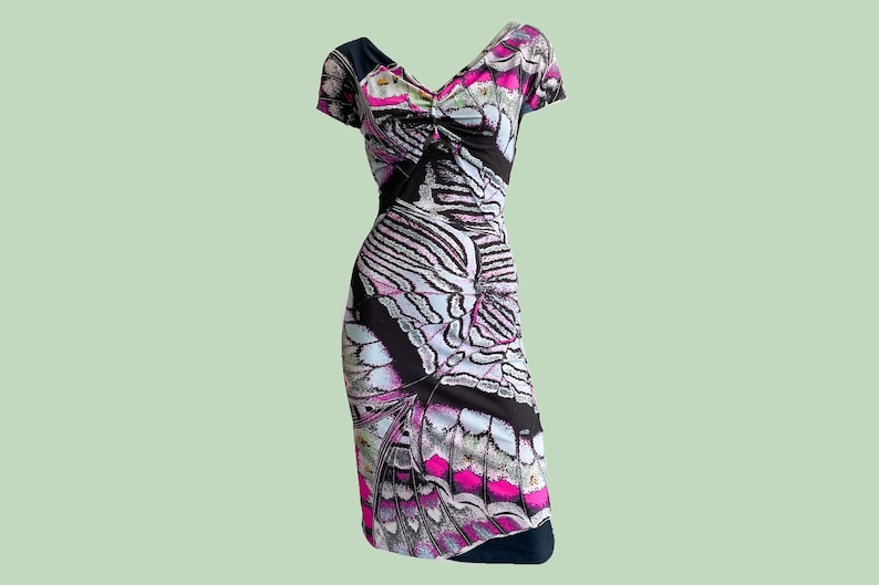 K&ouml;nnte beinhalten: Ein schwarzes, wei&szlig;es und pinkfarbenes Kleid mit einem Schmetterlingsmuster. Das Kleid hat einen V-Ausschnitt und kurze &Auml;rmel.