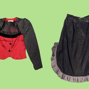 Op de afbeelding: Een vintage tweedelige outfit. De top is een rood-zwart gestreept vest met zwarte knopen en een zwarte bolero met rode stippen. De outfit bevat een zwarte rok met een gefranjerde zoom.