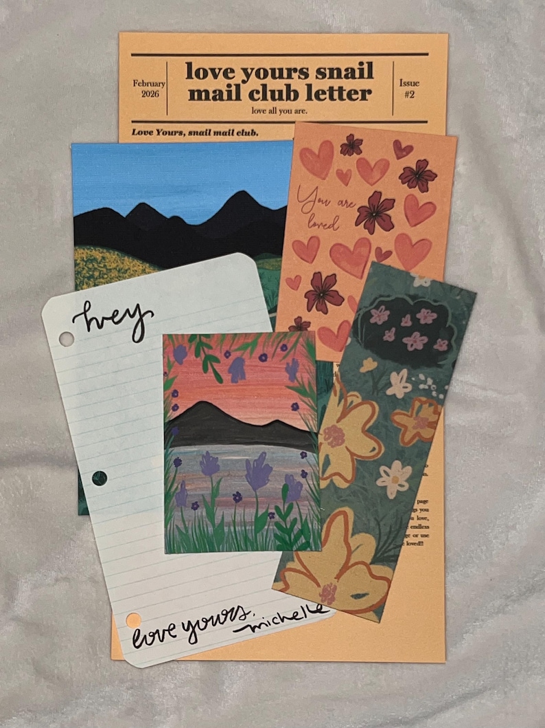 May include: A collection of stationery items including a peach-colored Love Yours Snail Mail Club letter, a landscape print with mountains, a card with hearts and the text You are loved, a lined paper with the word hey and love yours michelle, and a floral bookmark.