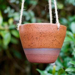 May include: A brown speckled hanging planter with a light brown band around the top. The planter is hanging from a natural twine cord.