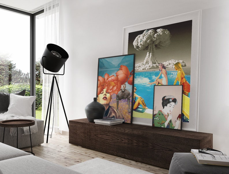 May include: A living room interior with a wooden shelf displaying three framed art prints. The prints feature a collage of a woman with flowers, a scene of people swimming in a pool with an atomic bomb explosion in the background, and a traditional Japanese woman in a kimono.