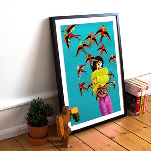 May include: A woman in a yellow sweater and pink pants is surrounded by colorful birds on a turquoise background. The birds are flying in different directions and some are landing on her. The woman is smiling and has her arms wrapped around herself.