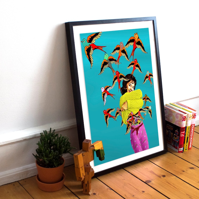 May include: A woman in a yellow sweater and pink pants is surrounded by colorful birds on a turquoise background. The birds are flying in different directions and some are landing on her. The woman is smiling and has her arms wrapped around herself.