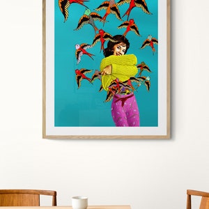 May include: A woman in a yellow sweater and pink patterned pants stands in front of a turquoise background. She is surrounded by a flock of colorful birds with red, yellow, blue, and green accents.