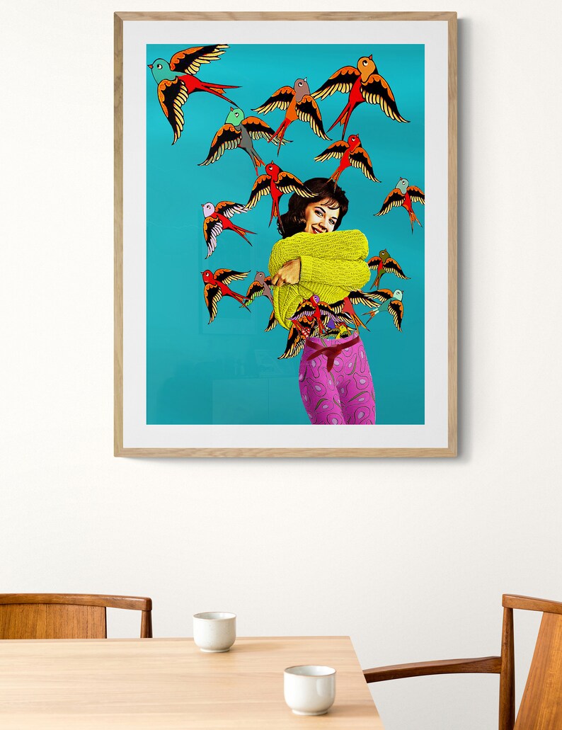 May include: A woman in a yellow sweater and pink patterned pants stands in front of a turquoise background. She is surrounded by a flock of colorful birds with red, yellow, blue, and green accents.