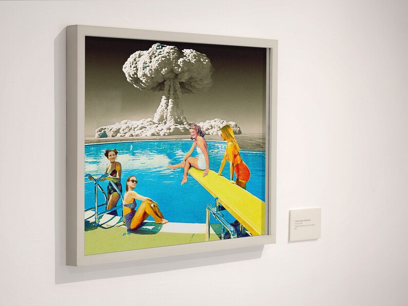 May include: A framed collage artwork depicting four women in swimsuits by a pool with a mushroom cloud in the background. The women are on a diving board and in the pool. The artwork is in a white frame.