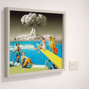 May include: A framed collage artwork depicting four women in swimsuits by a pool with a mushroom cloud in the background. The women are on a diving board and in the pool. The artwork is in a white frame.