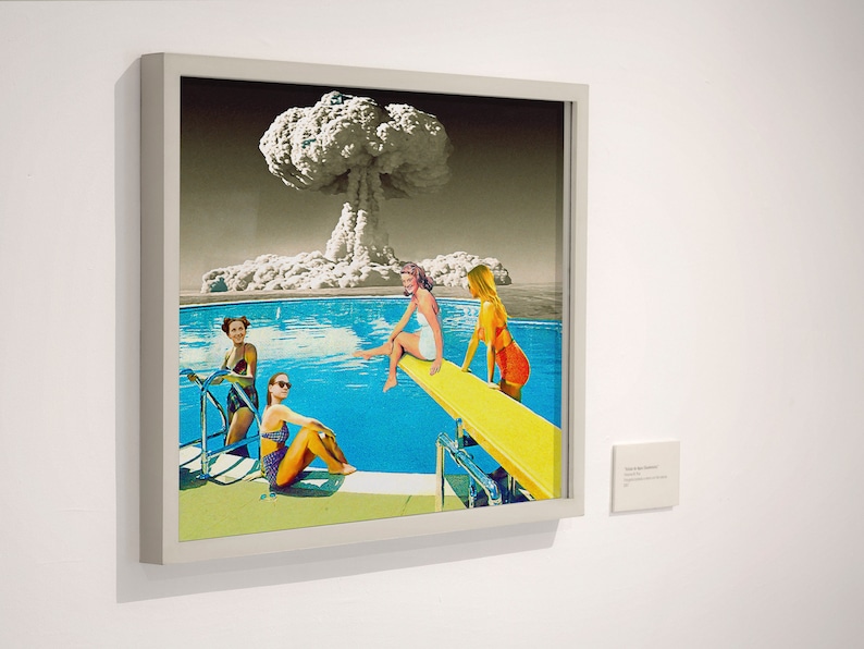 May include: A framed collage artwork depicting four women in swimsuits by a pool with a mushroom cloud in the background. The women are on a diving board and in the pool. The artwork is in a white frame.