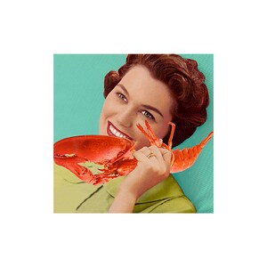 May include: A woman with red hair is holding a red lobster in front of her mouth. She is smiling and looking at the camera. The background is a light blue color.