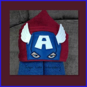 Puede incluir: Una toalla de ba&ntilde;o con capucha en rojo y azul, con un dise&ntilde;o de Capit&aacute;n Am&eacute;rica. La toalla tiene una m&aacute;scara azul con una "A" blanca y alas blancas. El texto "Sugar Lake Embroidery" es visible en la toalla azul.