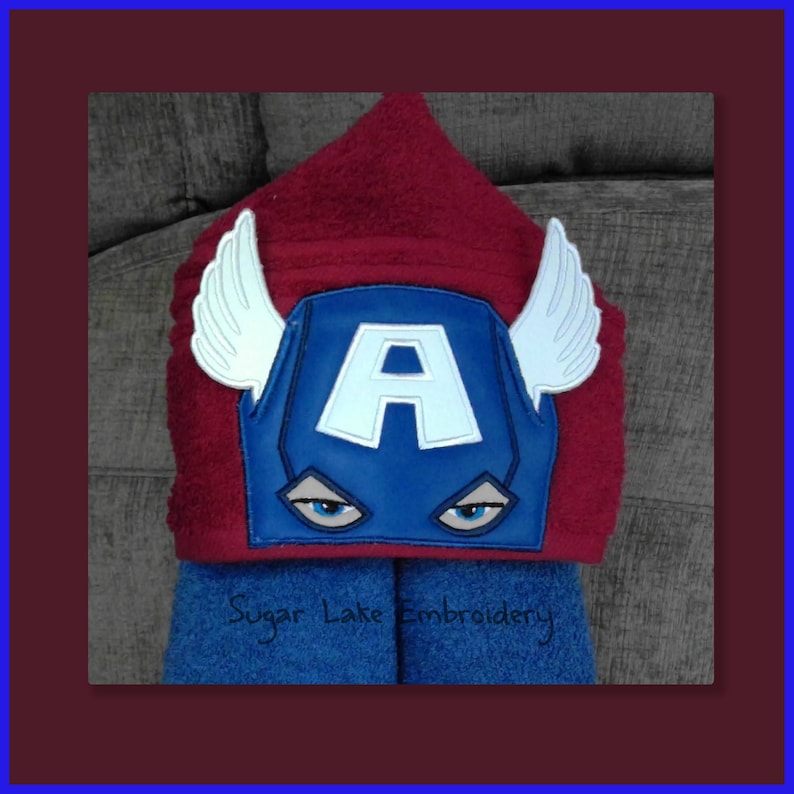 Puede incluir: Una toalla de ba&ntilde;o con capucha en rojo y azul, con un dise&ntilde;o de Capit&aacute;n Am&eacute;rica. La toalla tiene una m&aacute;scara azul con una "A" blanca y alas blancas. El texto "Sugar Lake Embroidery" es visible en la toalla azul.