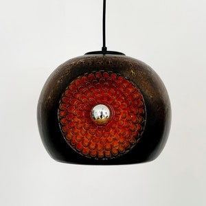 Könnte beinhalten: Eine braune und orangefarbene Globus-Pendelleuchte mit silbernem Zentrum. Die Leuchte hängt an einem schwarzen Kabel.