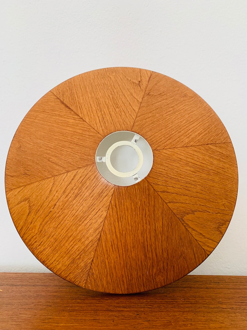 Puede incluir: Una pantalla de l&aacute;mpara redonda de madera con un acabado marr&oacute;n claro. La pantalla tiene una abertura central para una bombilla y un anillo de metal blanco alrededor de la abertura.