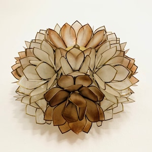 Op de afbeelding: Een decoratieve wandhanger gemaakt van overlappende, doorschijnende, beige en bruine bloemvormige stukken. De stukken zijn in een cirkelvormig patroon gerangschikt, waardoor een driedimensionaal effect ontstaat.