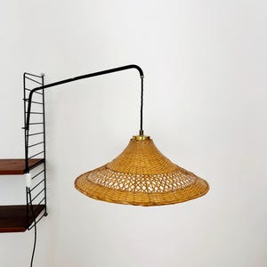 May include: A black metal wall-mounted lamp with a woven wicker shade. The lamp is extended out from the wall and has a black cord.