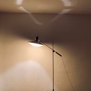 Puede incluir: Una l&aacute;mpara de escritorio negra ajustable con una pantalla blanca y una base de madera. La l&aacute;mpara est&aacute; sobre una mesa de madera.