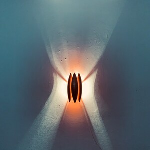 May include: A modern wall sconce with a warm, orange glow. The sconce is made of dark wood and has a unique, geometric design.