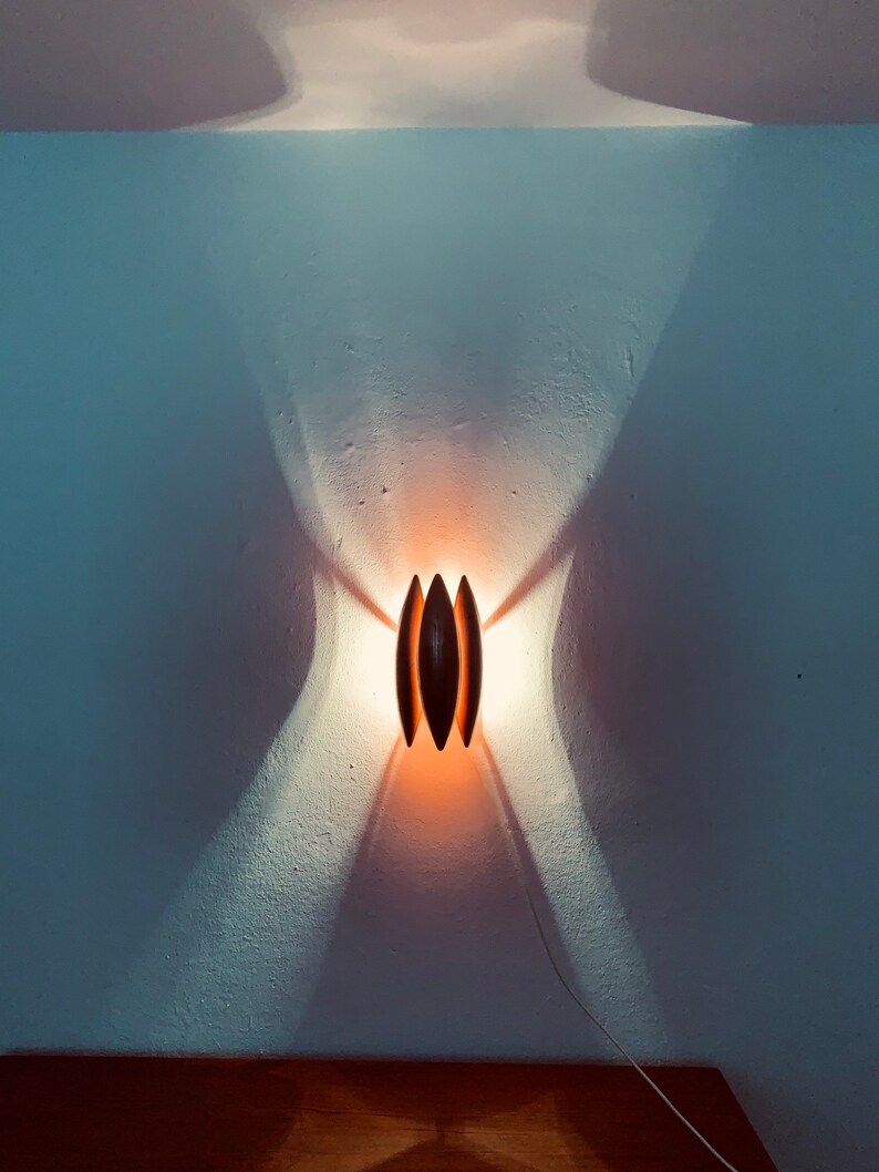 May include: A modern wall sconce with a warm, orange glow. The sconce is made of dark wood and has a unique, geometric design.