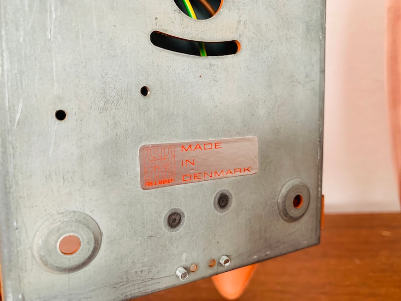 May include: Close-up of a metal back panel with a sticker that reads "MADE IN DENMARK". The panel has several holes and is a light gray color.