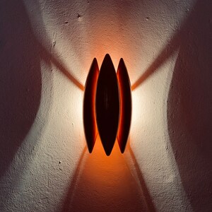 May include: A wall-mounted light fixture with three overlapping, oval-shaped shades. The shades are a dark brown color and the light casts a warm orange glow.