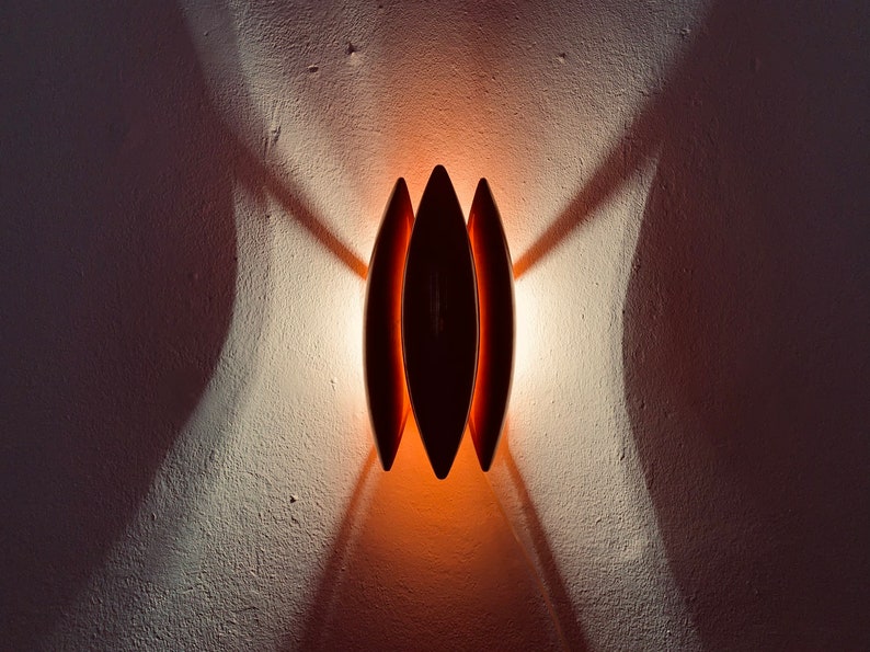 May include: A wall-mounted light fixture with three overlapping, oval-shaped shades. The shades are a dark brown color and the light casts a warm orange glow.