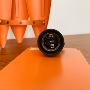 May include: Close-up of a black electrical socket with a metal center. The socket is on a wooden surface.